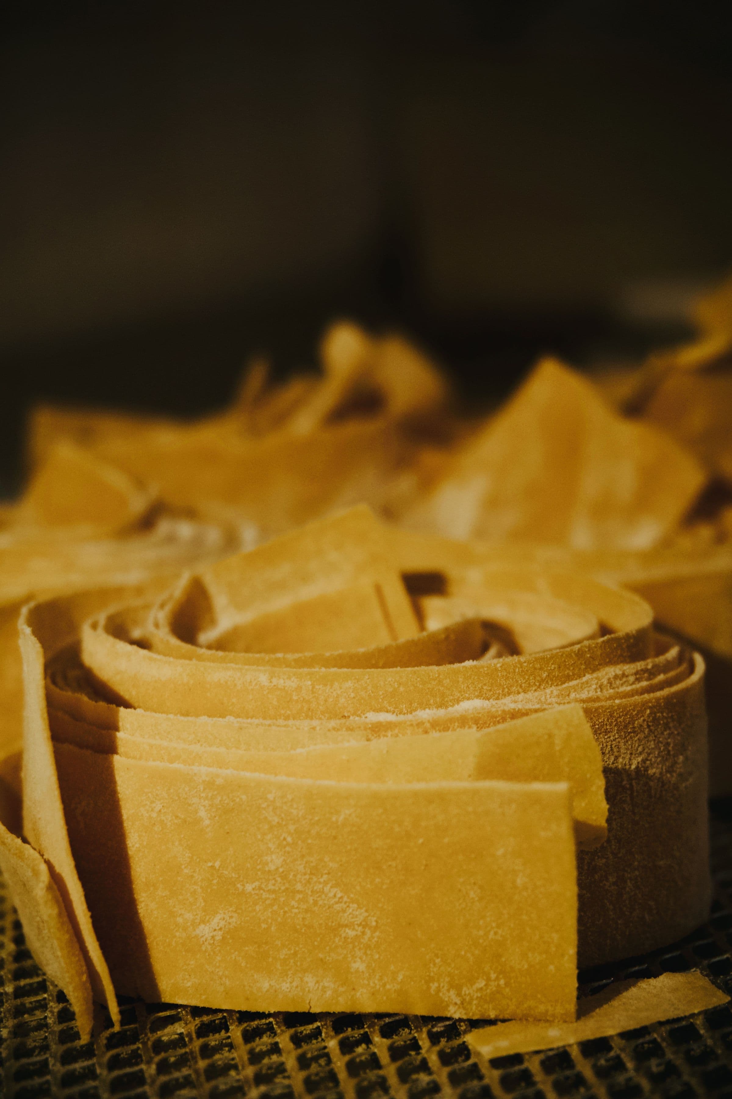 Nests of fresh pappardelle ribbons dusted with flour on a drying rack