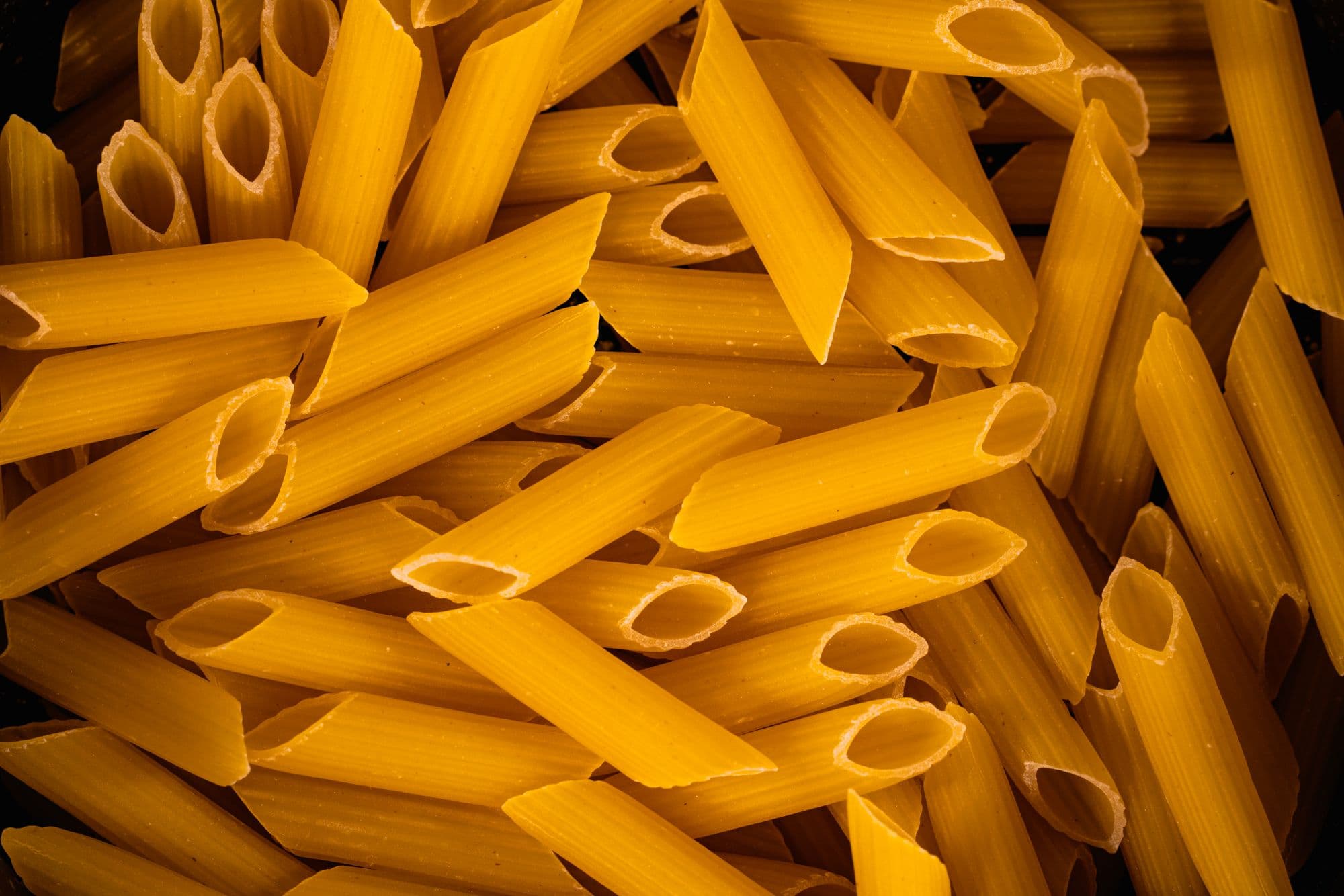 A close-up pile of dried penne rigate, the diagonally cut ends and ridges filling the frame