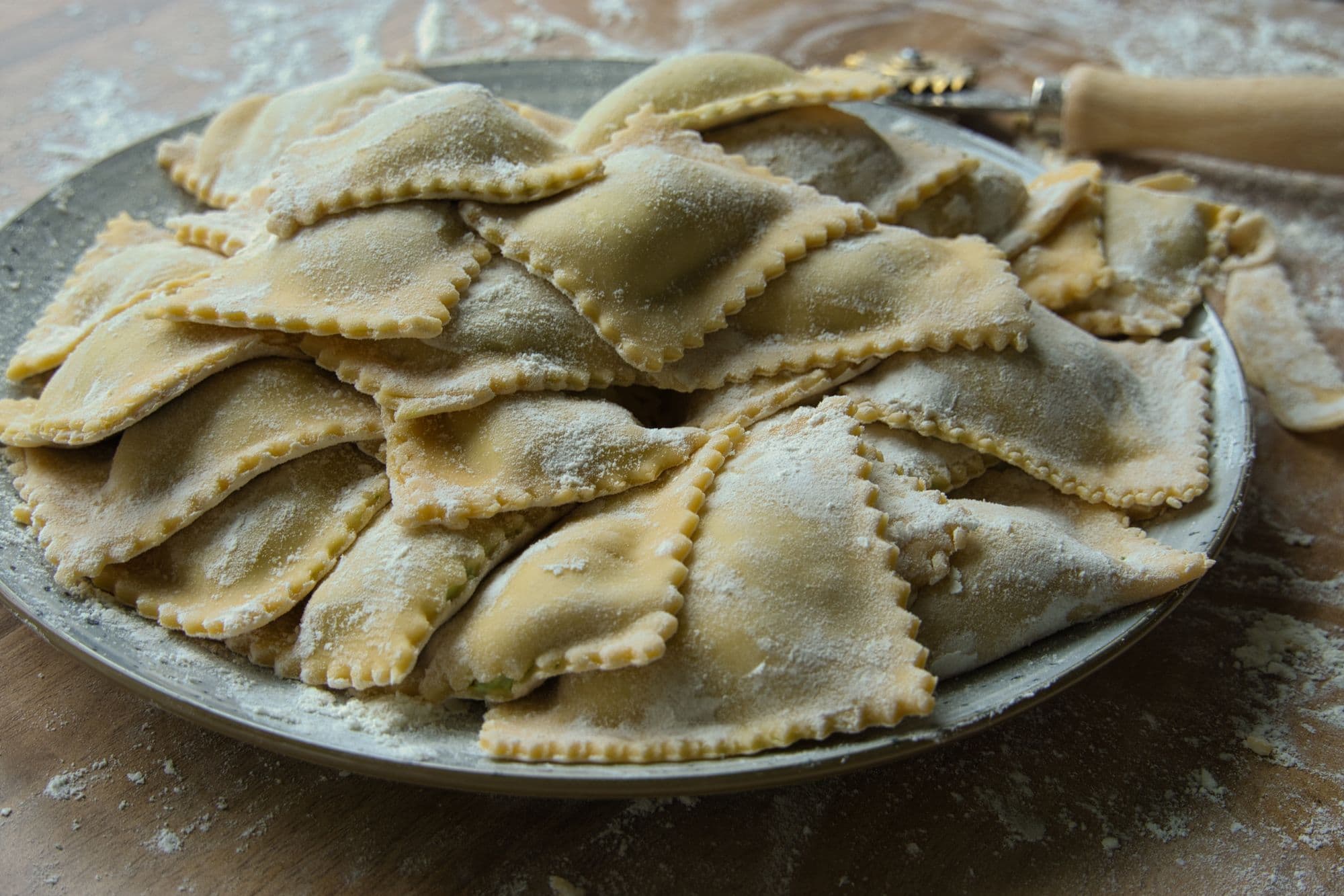 Raw, flour-dusted ravioli with crimped edges piled on a rustic plate