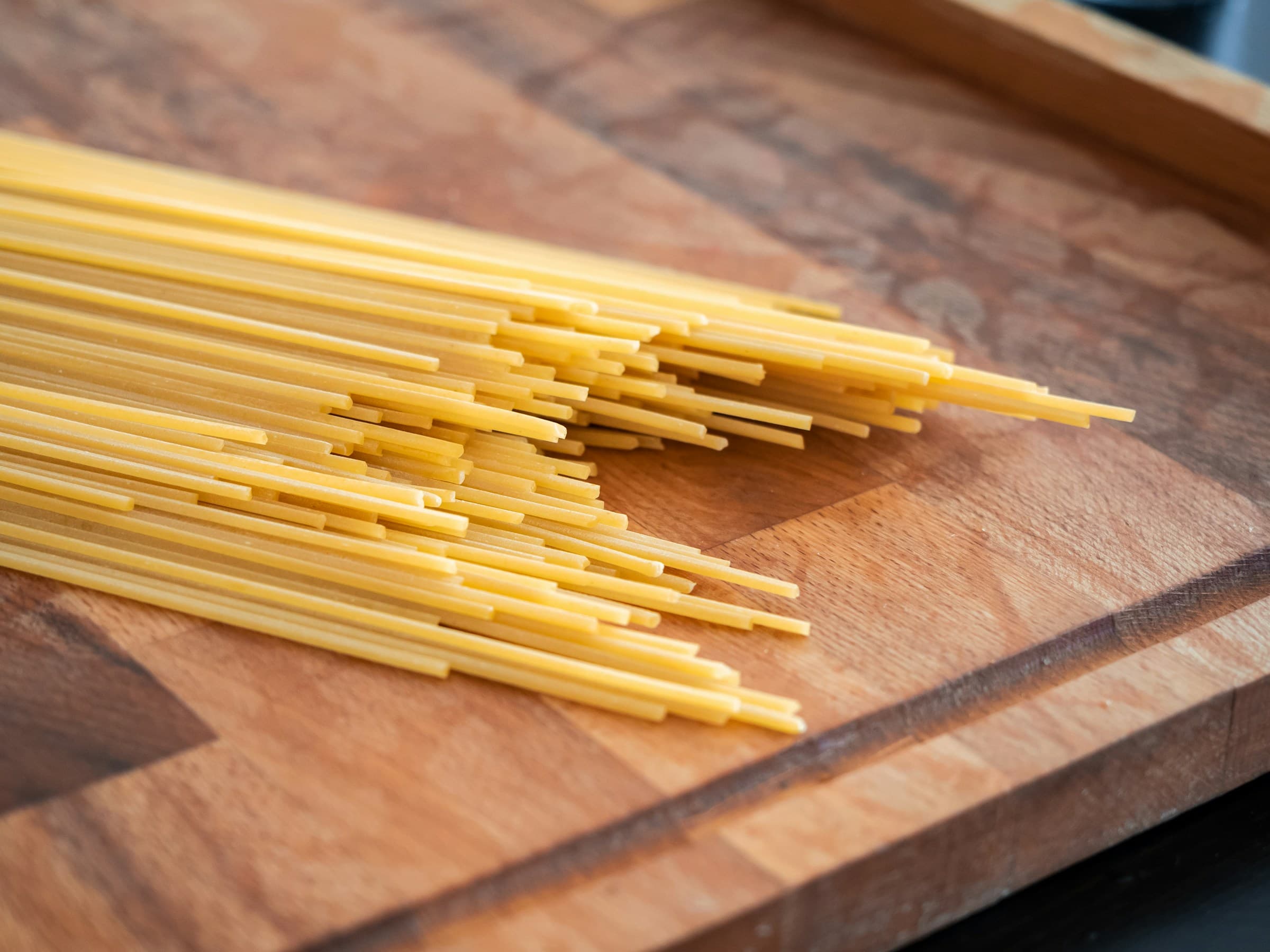 Dried spaghetti strands fanned out on a wooden cutting board